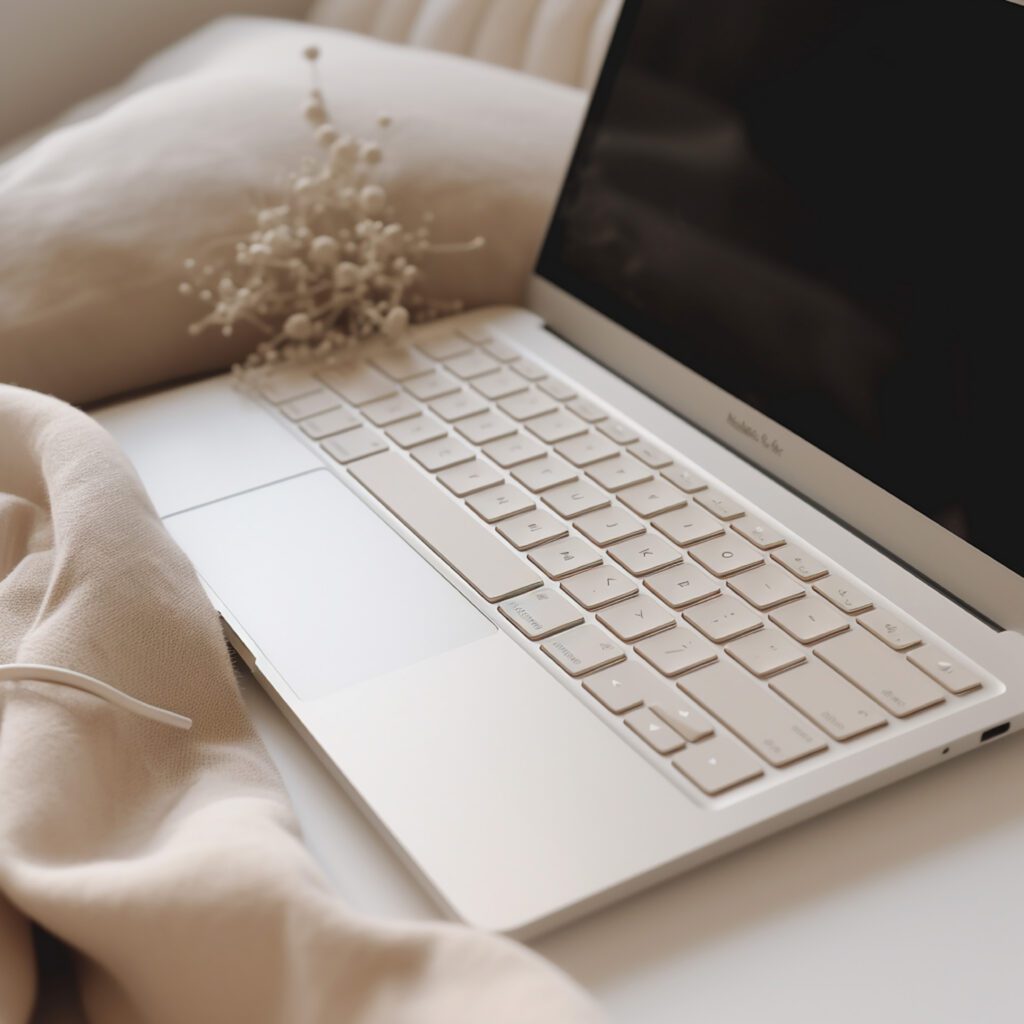 Beige laptop with white keys on a soft pink blanket with a sprig of lady's breath, representing small business marketing solutions.