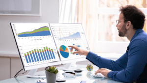 A man at a desk with two large monitors displaying predictive analytics data for SMBs