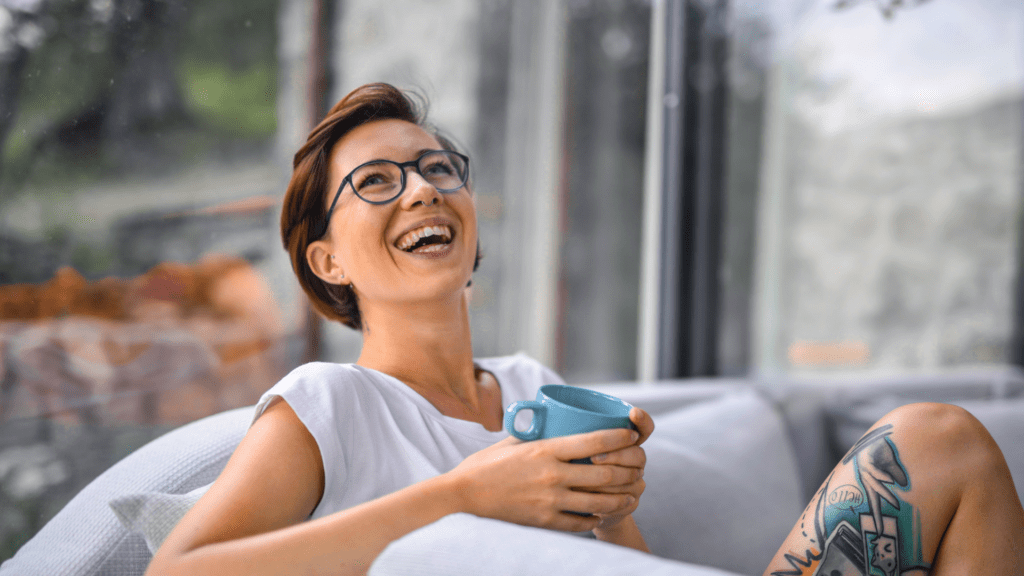 Woman on a couch with a cup of coffee, head thrown back in joy as an example of the role of emotional triggers in consumer behavior