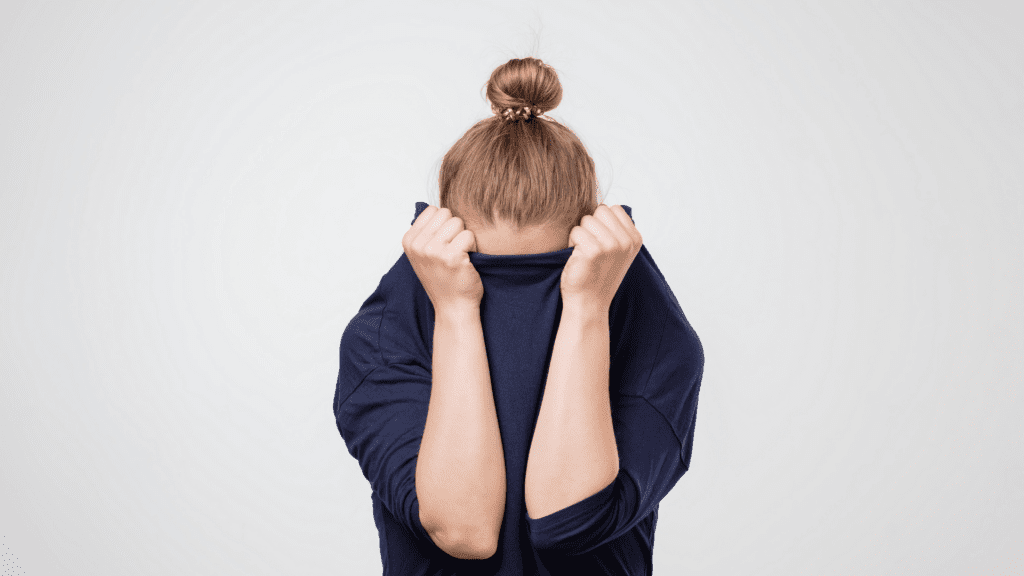 Woman hiding her face in a navy blue sweater, showing fear as an example of the role of emotional triggers in consumer behavior