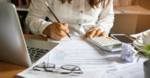 Woman in a white professional shirt working at a desk with budget and ROI spreadsheets in front of her, focusing on advertising budget optimization.